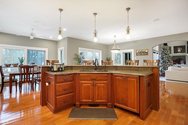 kitchen featuring sink, hanging light fixtures, ceiling fan, an island with sink, and stone countertops