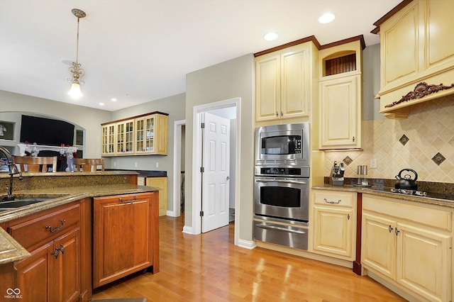 kitchen with pendant lighting, dark stone counters, sink, light hardwood / wood-style floors, and stainless steel appliances