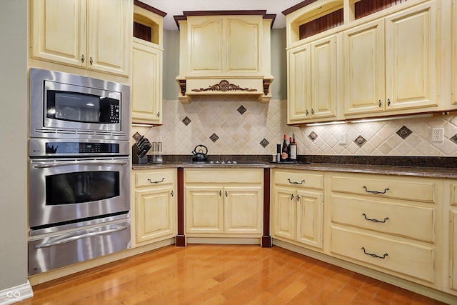 kitchen with stainless steel microwave, premium range hood, light hardwood / wood-style flooring, decorative backsplash, and dark stone countertops