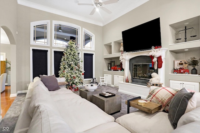 living room featuring ceiling fan, built in features, a high ceiling, and ornamental molding