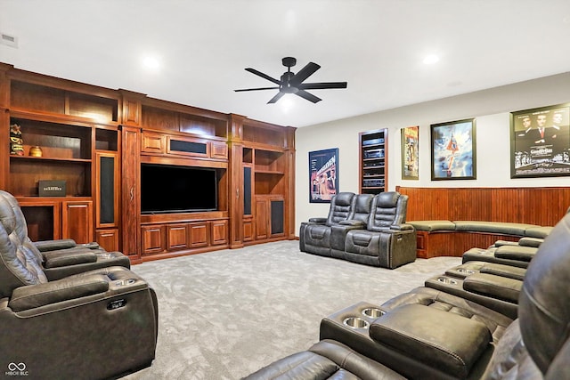 carpeted living room with built in shelves, ceiling fan, and wood walls