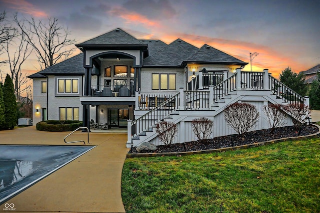 back house at dusk featuring a yard, a patio, and a covered pool