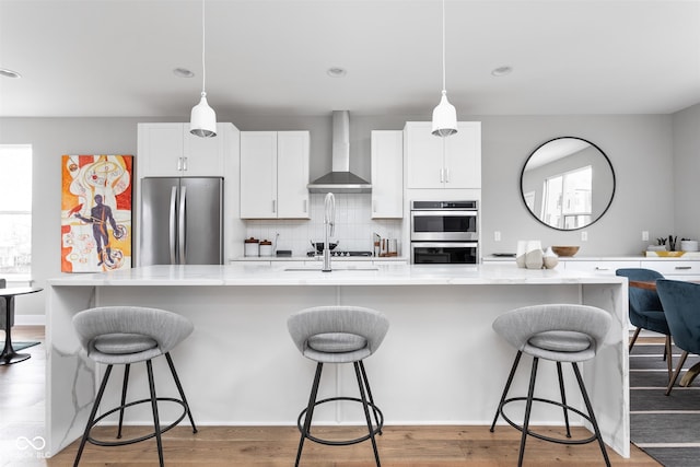 kitchen featuring white cabinets, appliances with stainless steel finishes, wall chimney exhaust hood, and a breakfast bar area