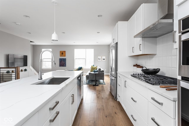 kitchen featuring stainless steel appliances, sink, wall chimney range hood, wood-type flooring, and white cabinets