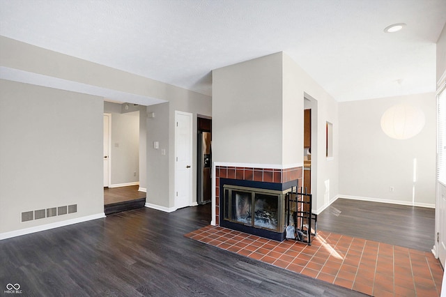 living room featuring a textured ceiling, dark wood-type flooring, and a tiled fireplace