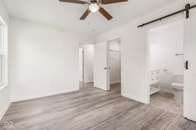 unfurnished bedroom featuring connected bathroom, a closet, ceiling fan, light hardwood / wood-style flooring, and a barn door