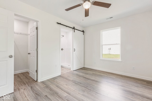 unfurnished bedroom featuring ceiling fan, a barn door, light wood-type flooring, a spacious closet, and a closet