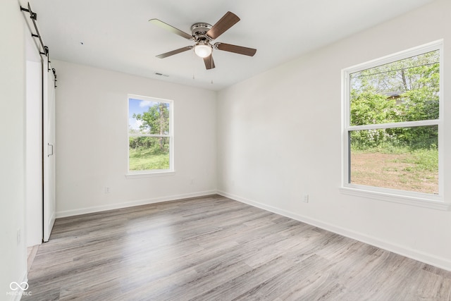 empty room featuring light hardwood / wood-style flooring, a barn door, and a healthy amount of sunlight