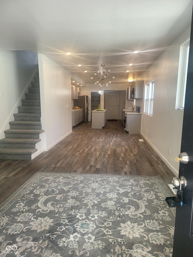 unfurnished living room featuring a notable chandelier, sink, and dark wood-type flooring