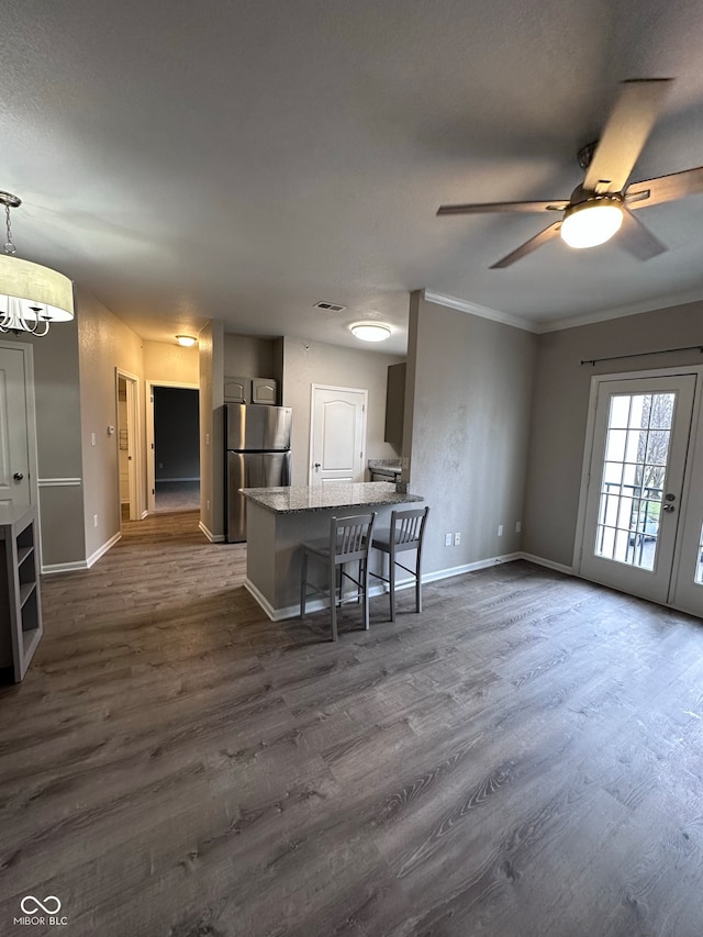 kitchen featuring ceiling fan with notable chandelier, dark hardwood / wood-style floors, stainless steel fridge, ornamental molding, and a breakfast bar area