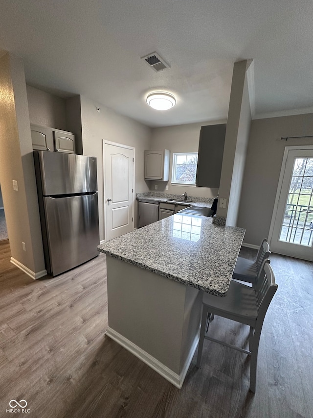 kitchen with appliances with stainless steel finishes, light wood-type flooring, gray cabinetry, and a healthy amount of sunlight