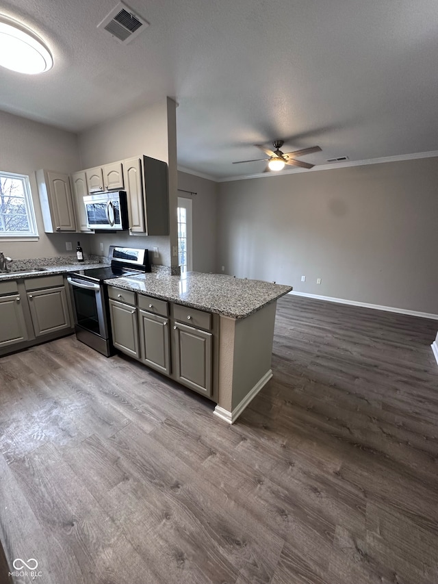 kitchen featuring light stone countertops, stainless steel appliances, kitchen peninsula, crown molding, and hardwood / wood-style floors