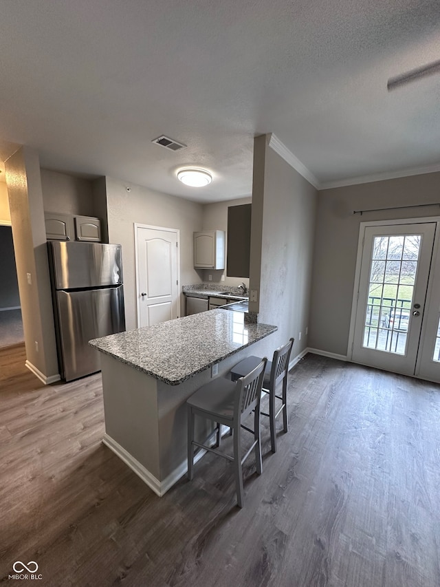 kitchen with kitchen peninsula, ornamental molding, gray cabinetry, dark wood-type flooring, and stainless steel refrigerator