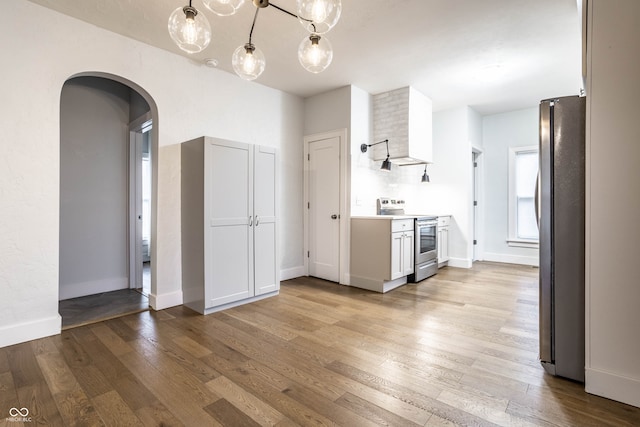 kitchen featuring white cabinets, appliances with stainless steel finishes, light hardwood / wood-style floors, and decorative light fixtures