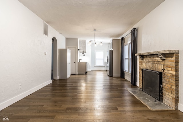 unfurnished living room featuring a chandelier, dark hardwood / wood-style flooring, and a brick fireplace