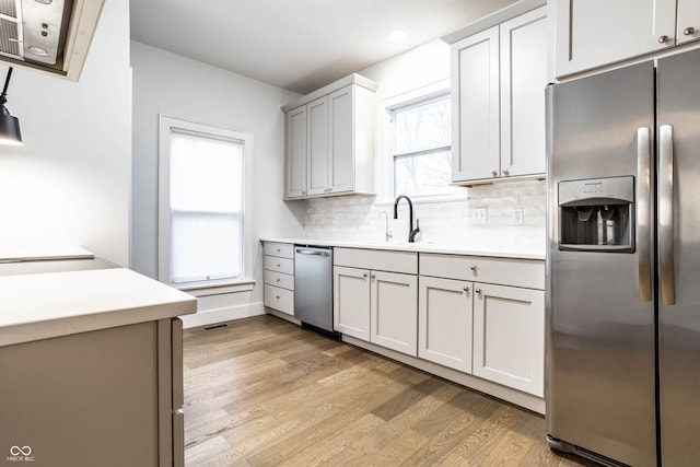 kitchen with backsplash, white cabinets, sink, light hardwood / wood-style flooring, and appliances with stainless steel finishes