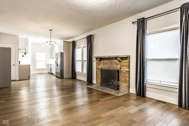 unfurnished living room with an inviting chandelier, wood-type flooring, a textured ceiling, and a brick fireplace