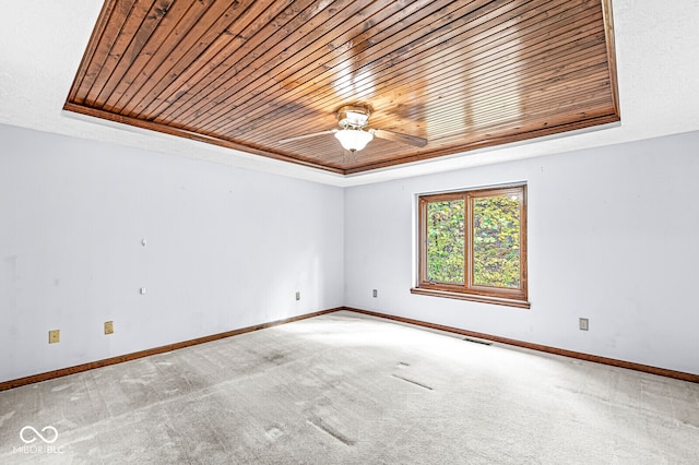 empty room with carpet flooring, a raised ceiling, and wooden ceiling