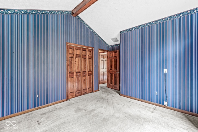 spare room featuring carpet, a textured ceiling, and vaulted ceiling with beams