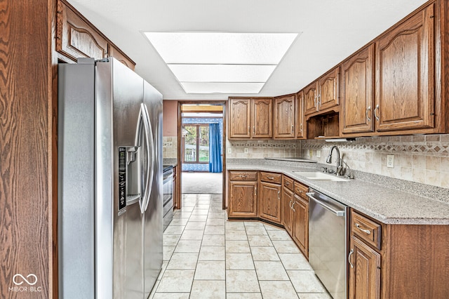 kitchen featuring appliances with stainless steel finishes, backsplash, a skylight, sink, and light tile patterned flooring