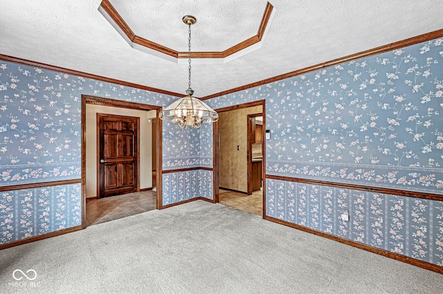 carpeted spare room with an inviting chandelier, a textured ceiling, and ornamental molding