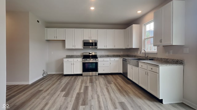 kitchen featuring sink, light stone counters, light hardwood / wood-style flooring, white cabinets, and appliances with stainless steel finishes