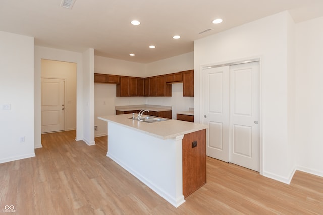 kitchen featuring sink, light wood-type flooring, and a kitchen island with sink