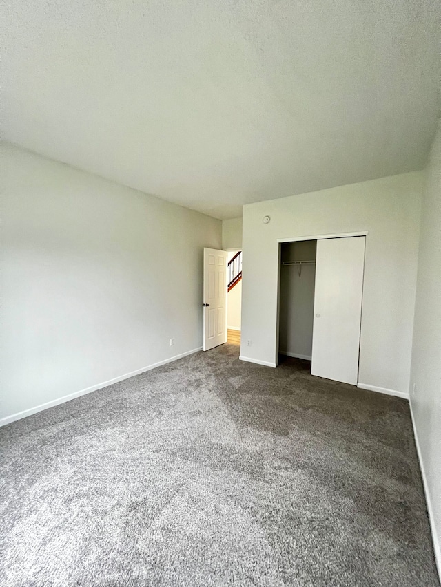 unfurnished bedroom with dark colored carpet, a textured ceiling, and a closet