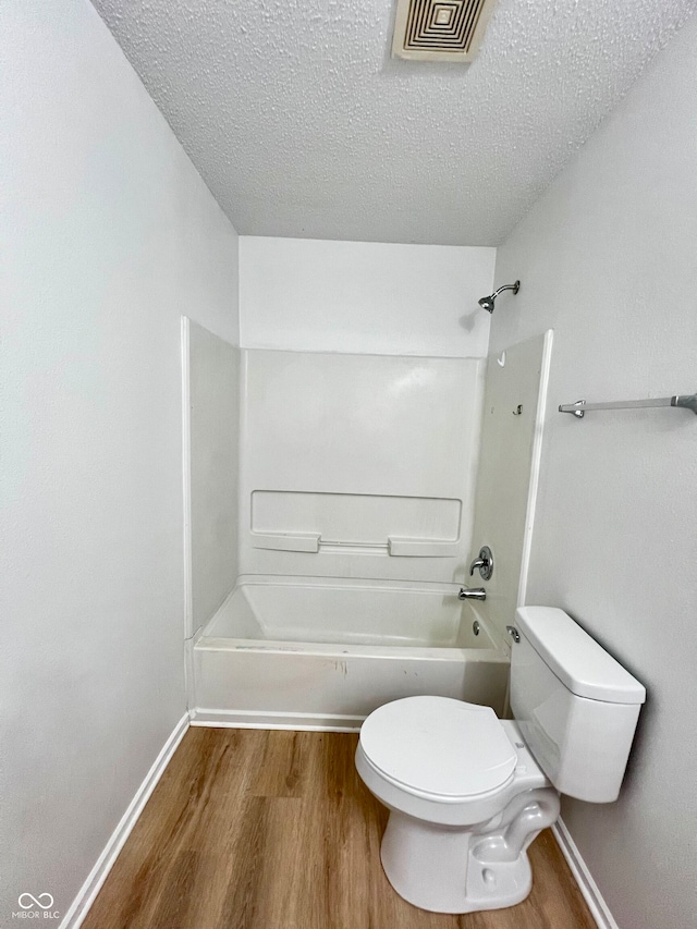 bathroom featuring wood-type flooring, a textured ceiling, bathing tub / shower combination, and toilet