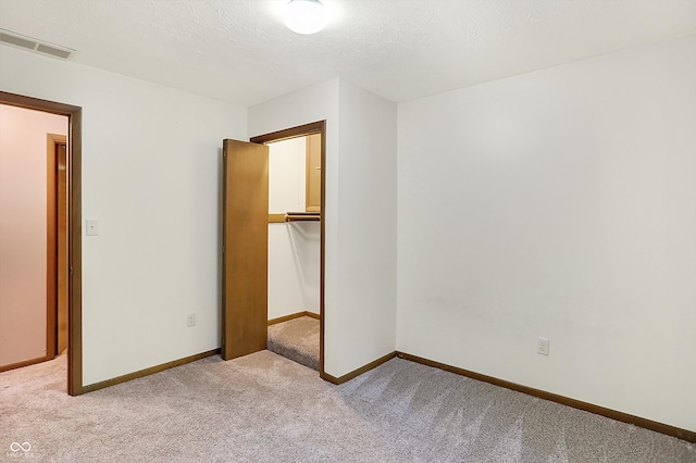 unfurnished bedroom with a textured ceiling, a walk in closet, light colored carpet, and a closet