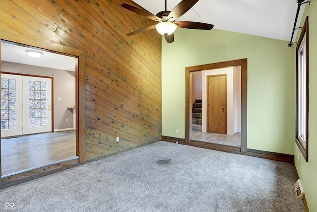 carpeted spare room featuring wood walls, ceiling fan, and lofted ceiling