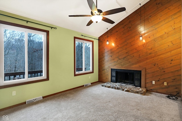 unfurnished living room featuring ceiling fan, wood walls, a stone fireplace, and carpet floors