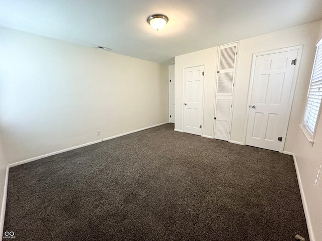 unfurnished bedroom with dark carpet and two closets