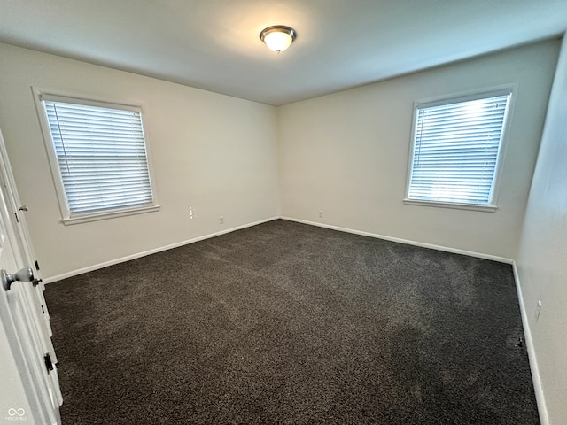 spare room with a wealth of natural light and dark colored carpet