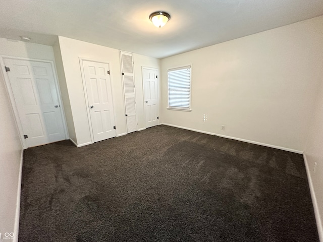 unfurnished bedroom featuring multiple closets and dark colored carpet