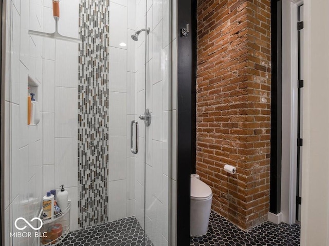 bathroom with tile patterned floors, toilet, a shower with door, and brick wall