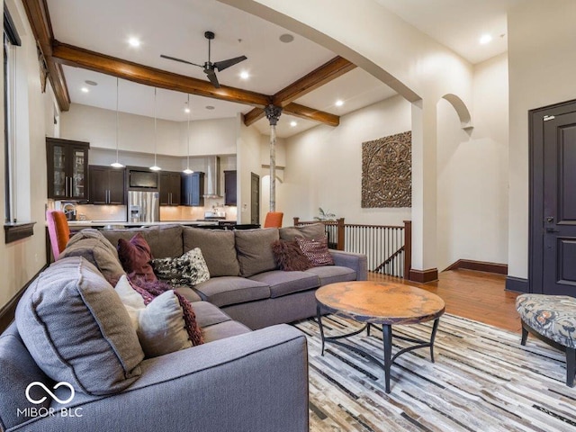 living room with ceiling fan, a towering ceiling, beamed ceiling, and light wood-type flooring