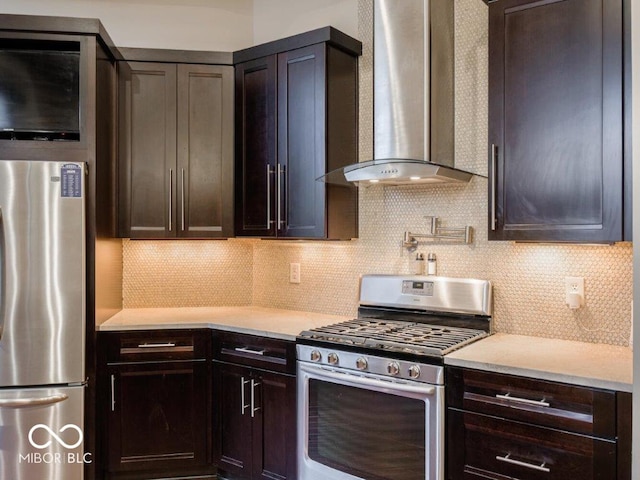 kitchen featuring wall chimney exhaust hood, dark brown cabinets, decorative backsplash, and appliances with stainless steel finishes