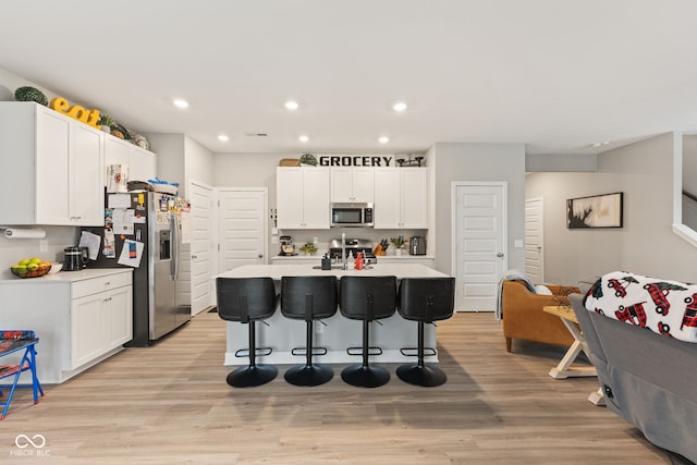 kitchen with a center island with sink, white cabinets, stainless steel appliances, and light hardwood / wood-style floors