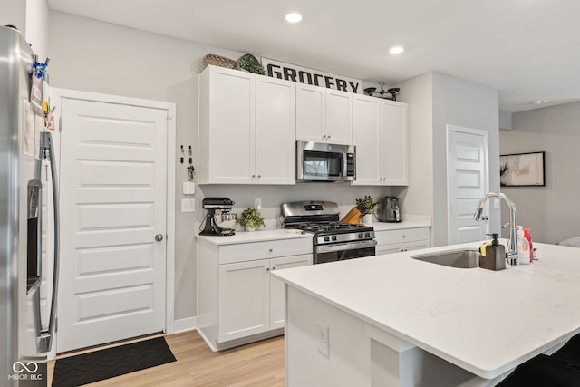 kitchen featuring a kitchen island with sink, white cabinets, sink, light wood-type flooring, and stainless steel appliances