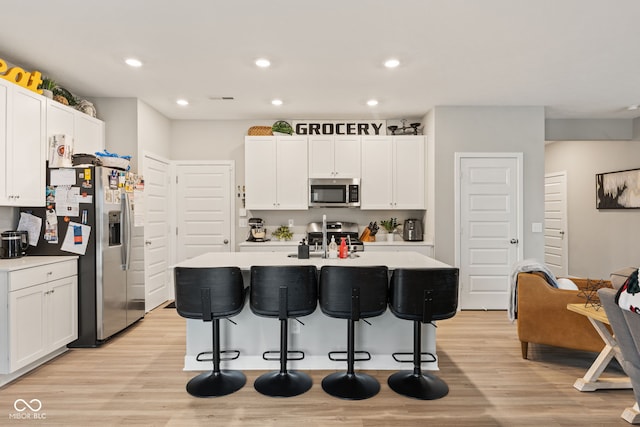 kitchen with white cabinetry, sink, stainless steel appliances, light hardwood / wood-style flooring, and a center island with sink