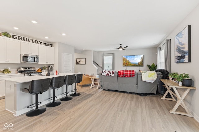 kitchen with a center island with sink, light wood-type flooring, appliances with stainless steel finishes, white cabinetry, and a breakfast bar area