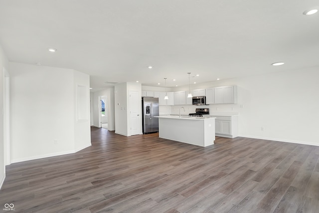 kitchen featuring hardwood / wood-style floors, white cabinets, a center island with sink, hanging light fixtures, and stainless steel appliances