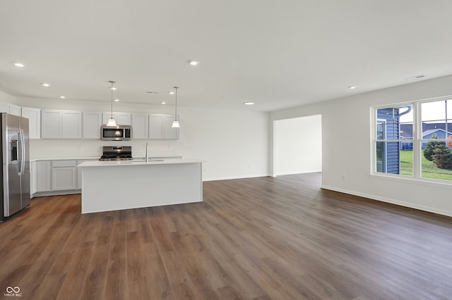 kitchen featuring appliances with stainless steel finishes, dark hardwood / wood-style flooring, decorative light fixtures, and an island with sink