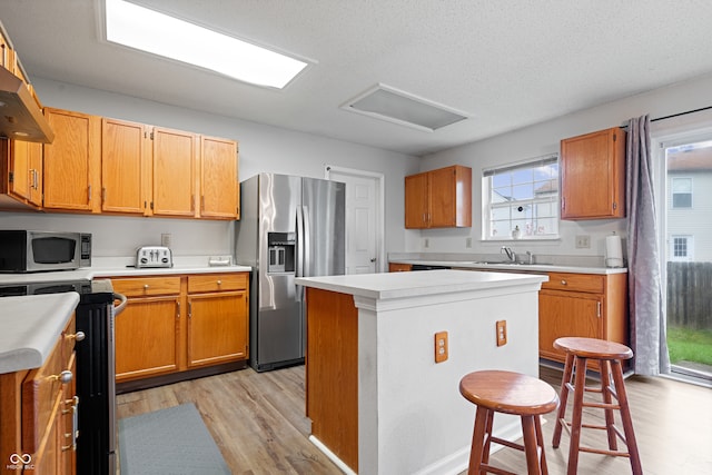 kitchen featuring a center island, sink, light wood-type flooring, a textured ceiling, and stainless steel appliances