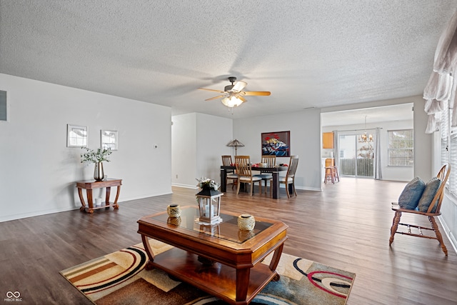 living room with dark hardwood / wood-style flooring, ceiling fan with notable chandelier, and a textured ceiling