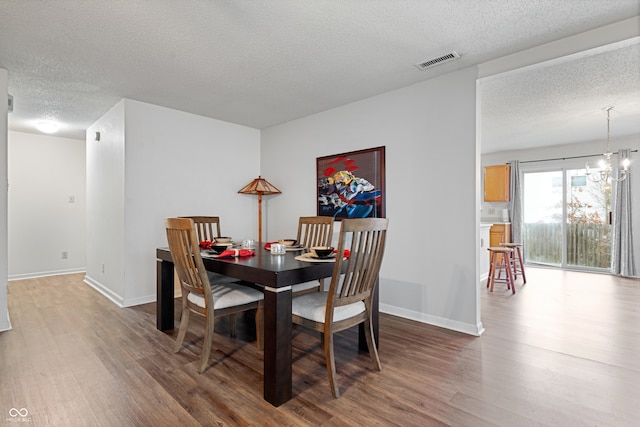 dining area featuring a notable chandelier, wood-type flooring, and a textured ceiling