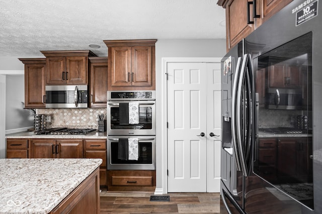 kitchen with light stone countertops, stainless steel appliances, dark hardwood / wood-style flooring, backsplash, and a textured ceiling