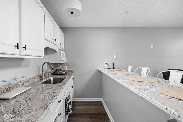 kitchen with white cabinetry, sink, dark wood-type flooring, light stone counters, and a textured ceiling