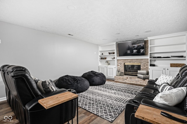 living room featuring built in features, dark wood-type flooring, a textured ceiling, and a brick fireplace